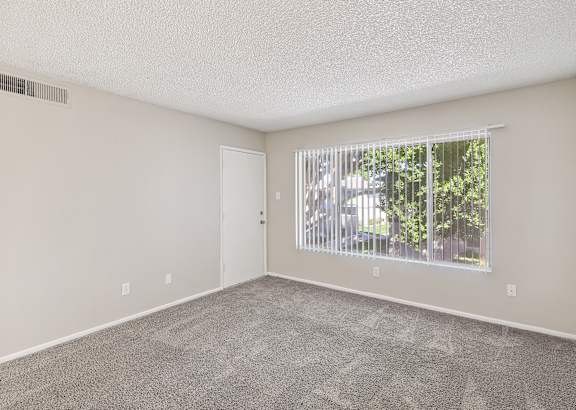 an empty living room with a large window and carpeting